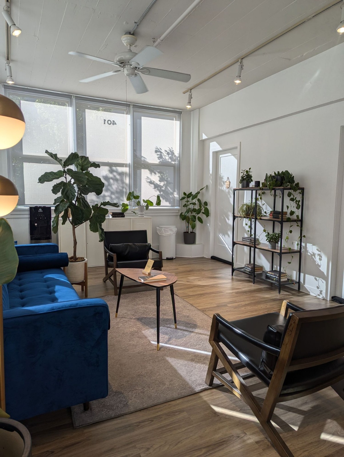 The in-person counselling room at Avery Therapy Centre — bright space with a blue velvet sofa, leather armchairs, plants, and natural light.